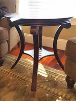 First photo showing the side table placed near seating, highlighting the curved legs and dark wood finish with some paint chipping.