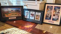 Three framed sports memorabilia shown placed on floor in front of white cabinets: from left to right, Boston Red Sox 2004 World Series ring ceremony panoramic photo and two framed Patriots championship photos in collage style.