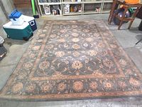 Full view of the wool area rug laid flat on a concrete floor in a storage-like area showing the full decorative design and wear condition.