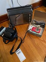 Lot showing Philco by Ford radio, Bushnell binoculars with neck strap, and boxed Canon PowerShot SD1200 IS camera with cables and manual.