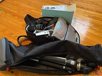 Open black camera bag containing Canon DSLR body with attached 18-55mm lens, additional 70-300mm lens, battery charger, remote switch and Hoya filter
