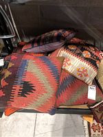 Seven southwestern tapestry throw pillows arranged on a shelf showing varied geometric and tribal designs and heavy wear.