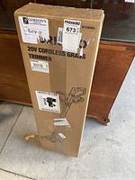 View of the full cardboard box showing the product title and line drawing of the grass trimmer, with some shipping labels attached.