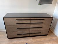 Front view of the Universal dresser showing six drawers with brown fronts and black handles against a black frame.