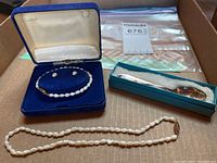 Full view of the pearl necklace laid out, pearl bracelet and earrings set inside blue velvet box, separate open box with silver Birks monogrammed spoon.