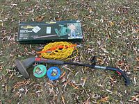 Full setup with hedge trimmer box, extension cord, weed wacker, and extra trimmer lines on grass.