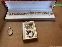 Photo showing a gold tone bracelet in Diamond Accent box, oval pendant, and birthstone pendant necklace in a small box