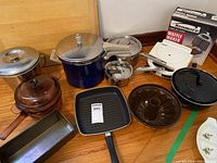 Photo of entire lot showing all items including cookware pots, pans, waffle maker in box, cutting board and bakeware