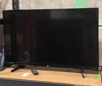 Front view of 43 inch LG flat screen TV with stand and remote on surface.