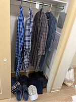 Photo showing 4 hanging men's housecoats in different plaid patterns, 4 pairs of folded pants, 5 pairs of joggers, one white hat, and pair of navy blue Crocs on floor.