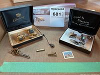 Overview photo of two sets of men's cuff links and tie clips in their original boxes with the items arranged on a table showing wear and vintage patina.