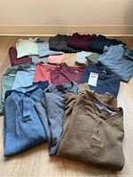 Group of 16 men’s long and short sleeve shirts laid out on floor in assortment of colors and styles.
