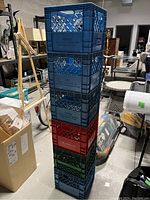 Full stack of eight assorted plastic milk crates in various colors including blue, black, red, and green, showing wear.