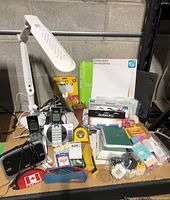 Overall view showing the VTech phones, desk lamp, measuring tapes, batteries, tape, writing pads, and other office supplies arranged on a table.