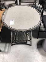 Front view of round faux wicker side table with glittery textured glass top, showing general condition and wicker damage.