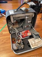 Open hard-sided case showing Pfaff 360 machine, manual, cord, pedal and assorted feet