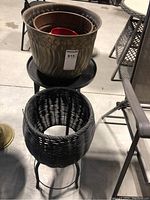 Various plant pots including large copper pots, black wicker plant stand, metal outdoor table/stand on display outdoors.