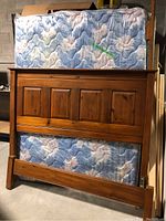 Full view of pine wood paneled headboard with mattress resting against it, mattress is blue floral quilted fabric design.