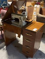 Sewing machine set inside a wooden vintage sewing desk with drawers and a hinge top revealing the machine