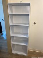 Front view of white pressboard shelving unit showing all shelves and adjustable holes.