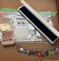 Photo showing sterling cubic zirconia earrings in pink and white velvet-lined box, sterling charm bracelet with multiple charms spread out on surface.