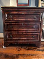 Front view of antique wooden veneer chest with three drawers, round metal knob pulls and keyhole escutcheons