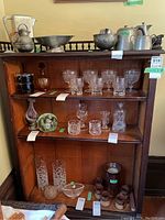 Front view of the wood bookshelf filled with various glassware and metal items, showing the shelves and interior space.