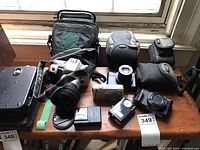 Overview of Minolta SLR, Fujifilm FinePix, Sony camera, light meter, cases and bag on wooden table