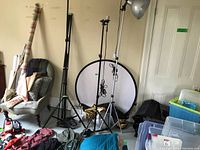 Wide view of corner space showing three adjustable metal light stands, collapsible background circle in rear, and some additional accessories on floor and chair.