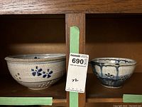 Two ceramic colanders placed on shelf, one larger beige with blue floral design, one smaller blue glaze colander