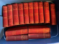 Photo showing 14 red cloth hardcover books by Charles Dickens with gold title and decoration on spines, arranged in two rows.