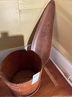 Wooden bucket missing metal strapping and tall carved wood centrepiece against wall.