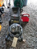Front view of the Craftsman lawn mower with Dust Blocker bag, red gas canister next to it, and manual placed on the mower.