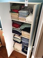 Full view of white cabinet containing folded linens and towels across four shelves in various colors including red, green, beige, blue, and gray.