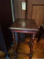 Overall view of the small wooden occasional table showing the worn top surface and turned legs.