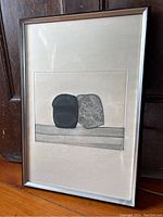 Full view of framed etching leaning against wood panel