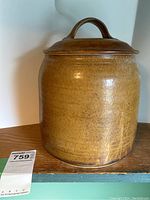 Front and side views of the brown glazed pottery crock with lid, showing its shape, glaze finish, and handle on the lid.