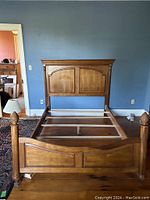 Full view of queen wooden bed frame assembled showing headboard, footboard, and rails in a room.