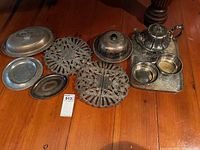Lot of silver plated items including teapot with lid on tray, two ornate trivets, butter dish with lid, small bowls, oval lid, and small tray. Items show tarnish and need cleaning.