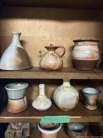 Shelf display of seven pottery items including three vases, three cups, and one canister, showing their size and glaze colors.