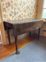 View of wooden table with two drop leaves closed, showing overall shape and aged surface.