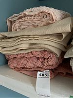 Stack of folded pink textured bedspreads and a wool blanket on a shelf.