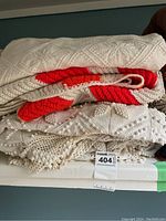 Stack showing two white vintage bedspreads with textured patterns and one folded red and white crocheted blanket on top.
