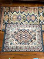 Photo showing both Turkish woven mats, the larger mat on top with fringes and geometric patterns in earthy tones, smaller mat below with central diamond and angular designs in muted colors.