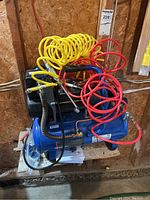 Blue Power Fist air compressor with yellow and red coiled hoses attached, set against wooden wall.