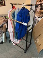 Clothing rack partially assembled with hangers and garments displayed, showing metal and plastic components