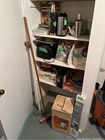 View of basement shelves with various kitchen items, cleaning tools including brooms, coffee percolator box, and window blinds box.