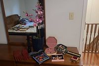 Full shot of the dresser showing red gloves, floral purse, pink artificial orchids in a pot, jewelry boxes, and black flashlight.