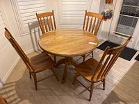 Photo showing round solid oak kitchen table with glass cover and four spindle back chairs arranged around it.