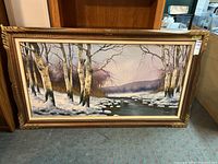 Full view of the framed landscape painting depicting snowy birch trees by a river, with signature and ornate wooden frame.